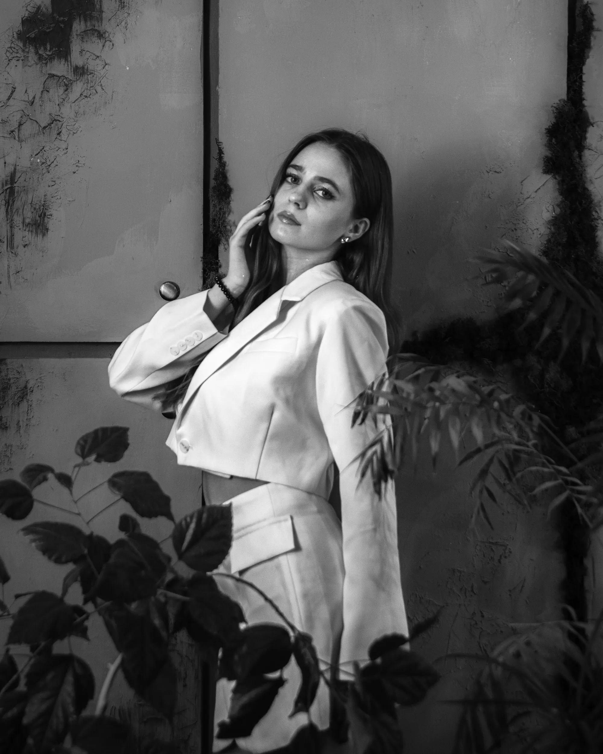 Woman in an ivory tailored suit in a softly lit interior with sculptural greenery